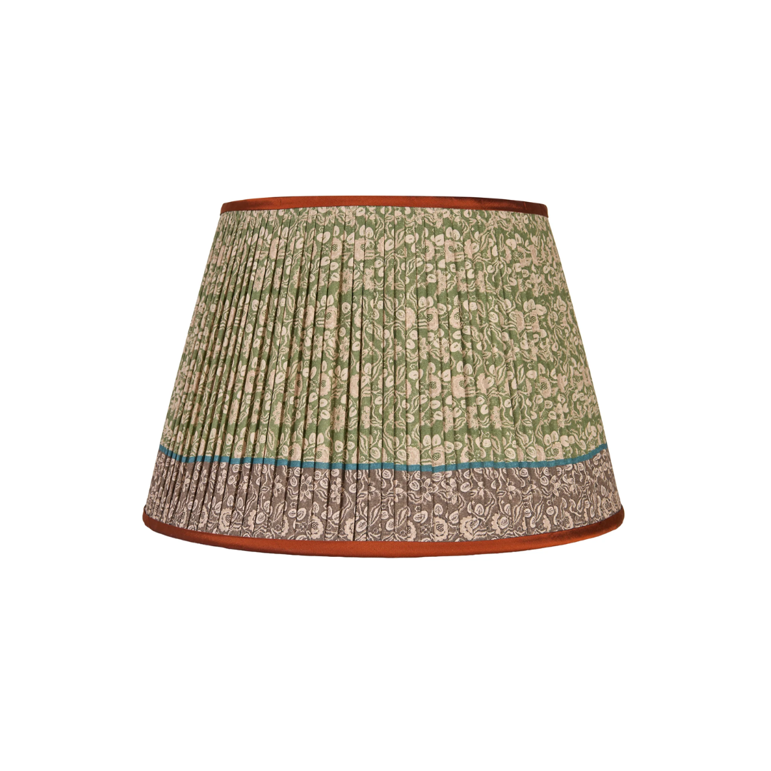 A pleated fabric Penny Morrison lampshade with a green and beige floral pattern, a thin turquoise stripe, and a brown patterned lower border, finished with a reddish-brown fabric rim.