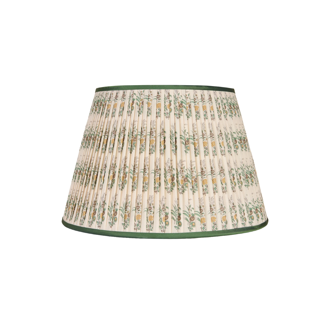 A pleated fabric penny morrison lampshade with a cream-colored background, a repeating green and yellow botanical pattern, and dark green trim at the top and bottom, shown against a plain white background.